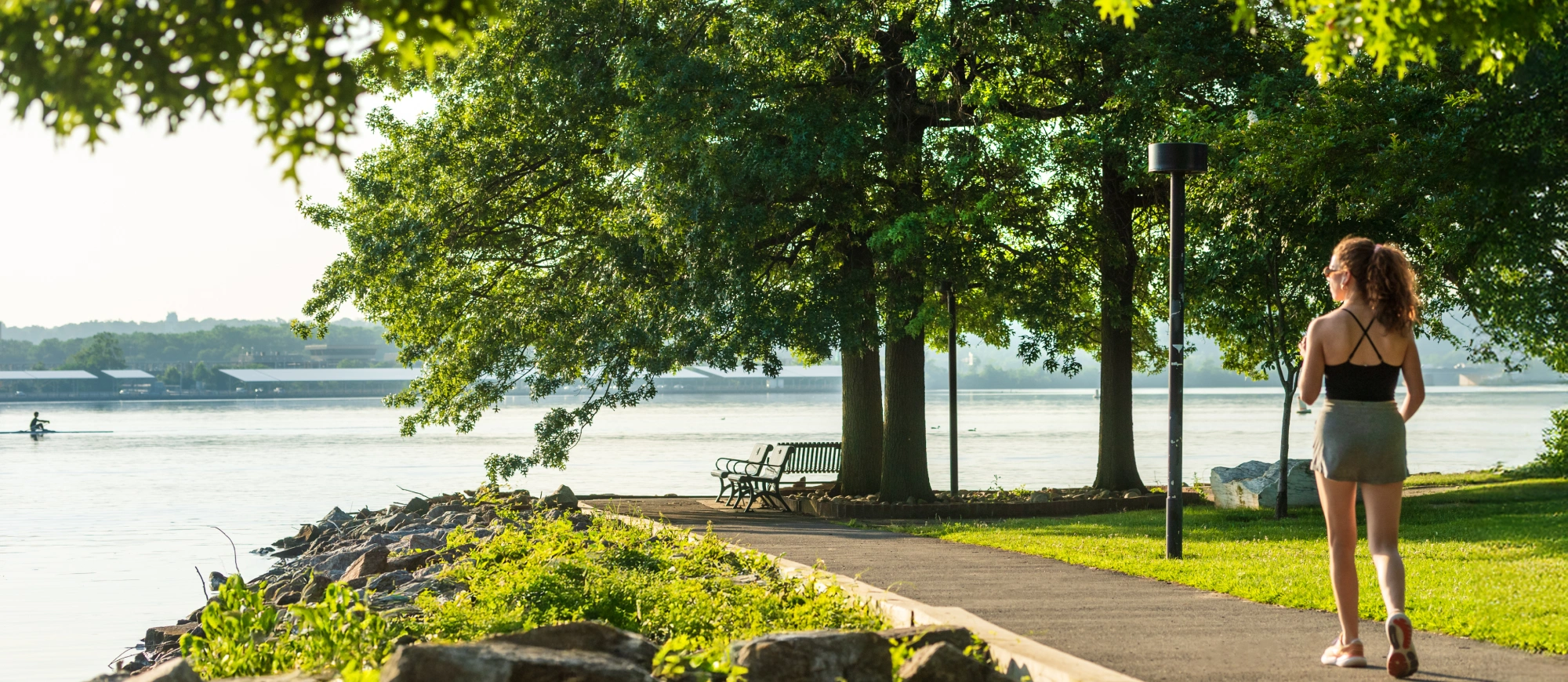 Woman walking on scenic riverside trail lined with trees and water views in the morning