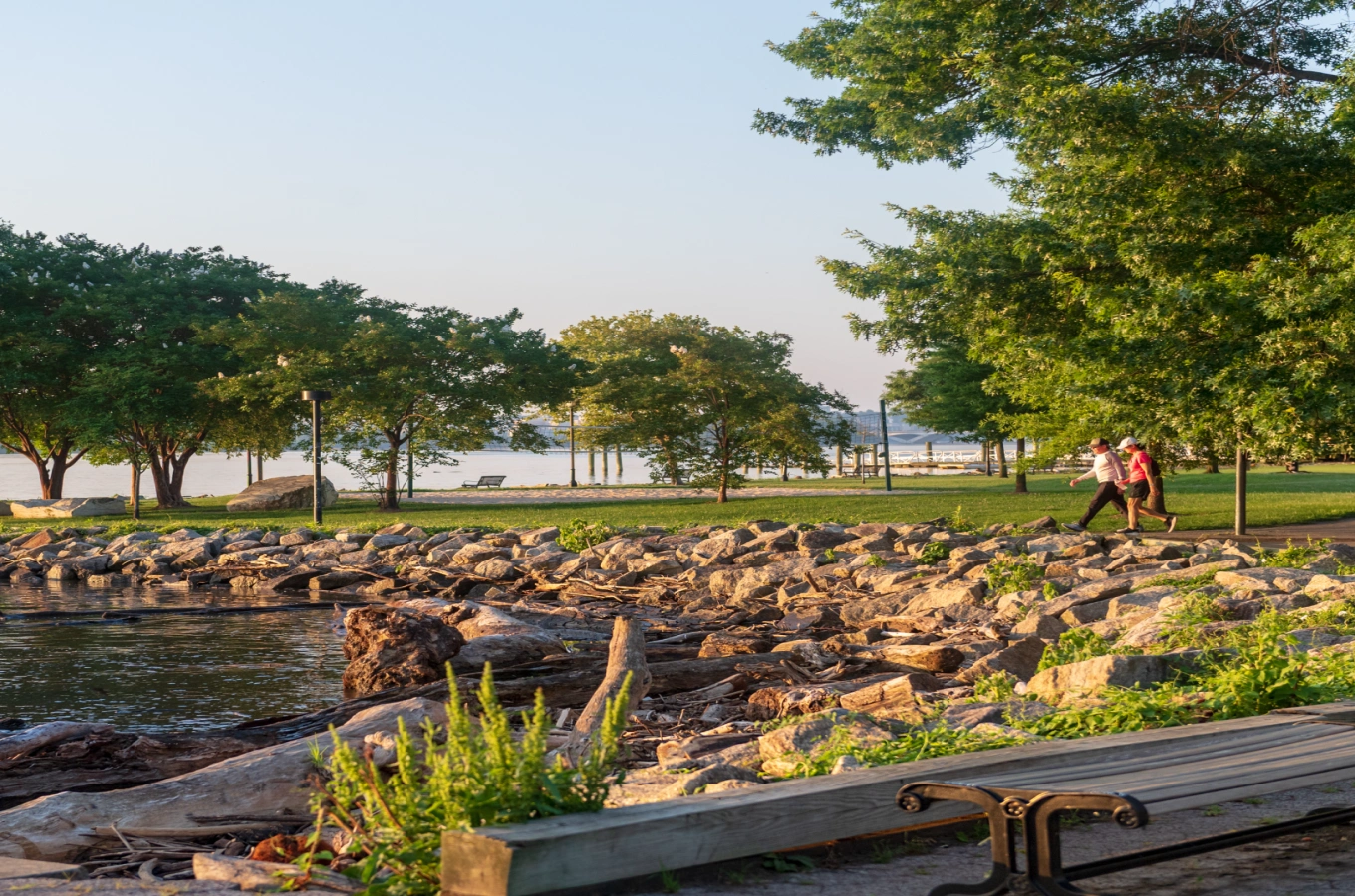 Peaceful nature setting with rocks, grassy areas, and people walking along waterfront trail