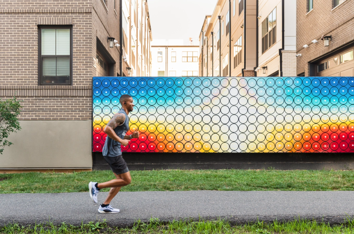 Man jogging past vibrant circular patterned wall mural in urban neighborhood with modern buildings