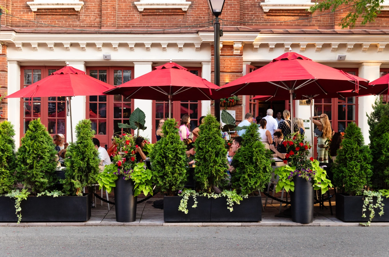 Outdoor dining area with red umbrellas and lush plants in front of historic brick building