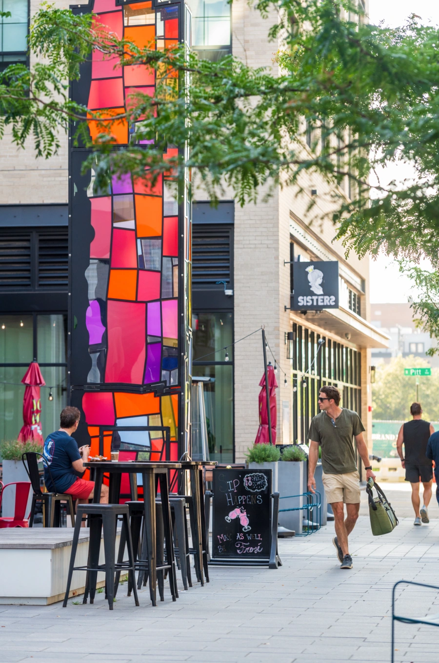 Man walking by vibrant urban art installation beside people dining at cafe tables