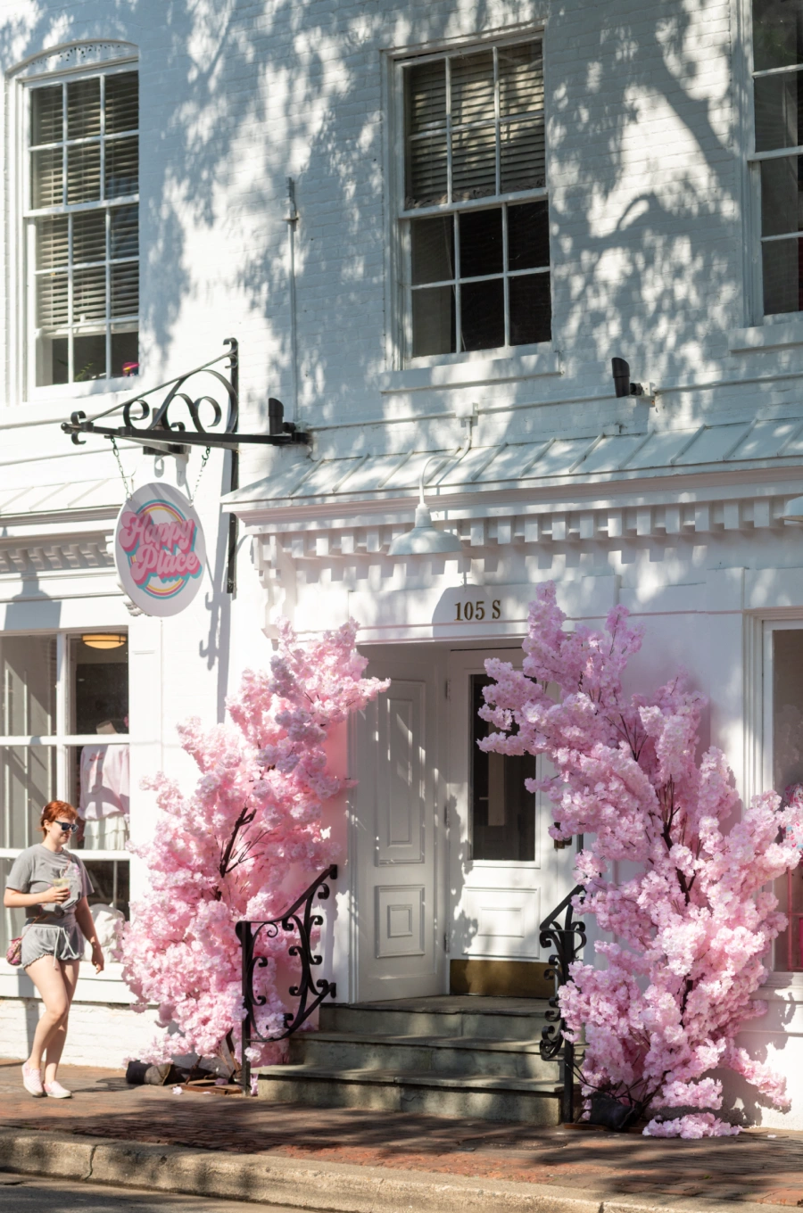 Boutique entrance decorated with pink cherry blossoms on sunny sidewalk morning stroll