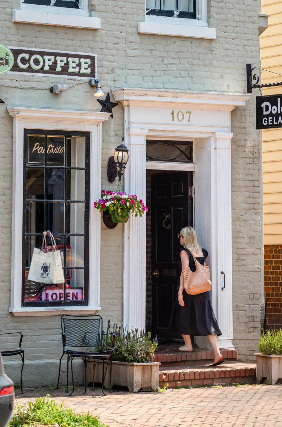 Woman entering vintage brick coffee shop with potted flowers and rustic sidewalk chairs