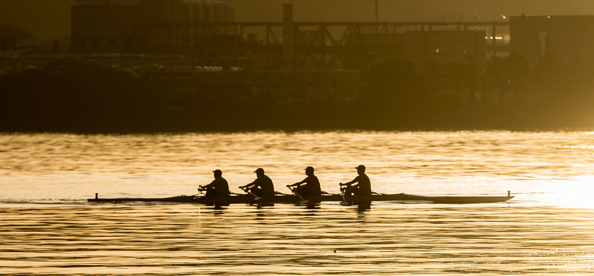 Rowing team gliding across Potomac River at sunrise with golden reflections on calm water