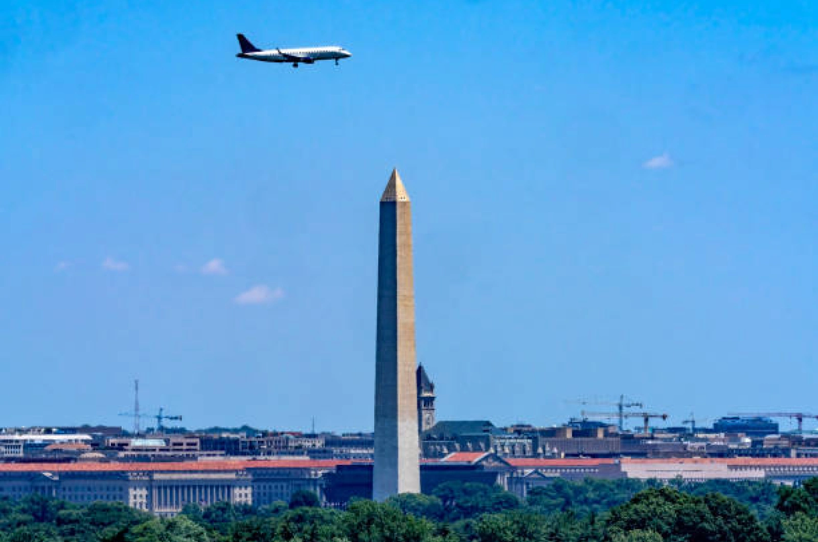 Airplane flying above Washington Monument against clear blue sky over downtown DC buildings