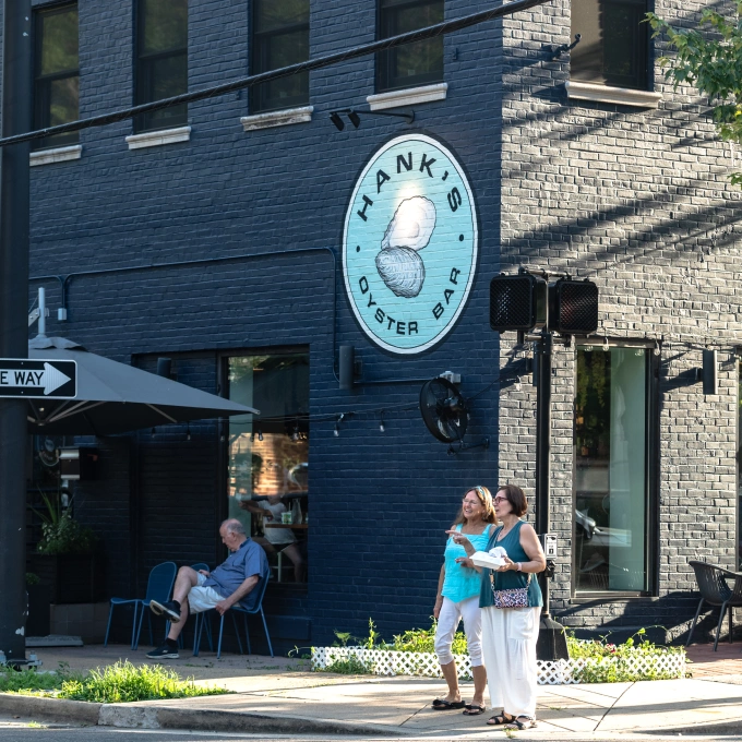 People enjoying sunny day near Hank’s Oyster Bar and its coastal-inspired street-side ambiance
